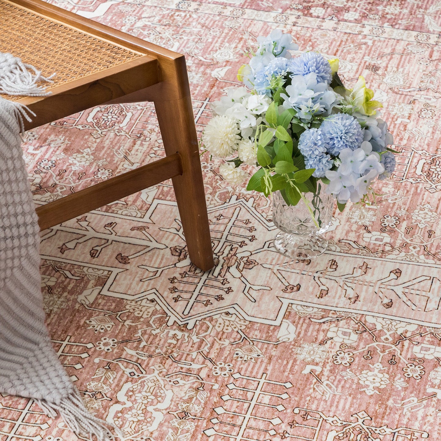 Floral arrangement on a patterned rug with a wooden chair and blanket.